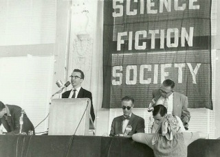 Here is Dave at NyCon II, sitting with bow tie and dark glasses; Larry Shaw at podium, John Campbell and Robert Silverberg to Kyle's left. Porter says, "Not my photo; I was 10 years old."